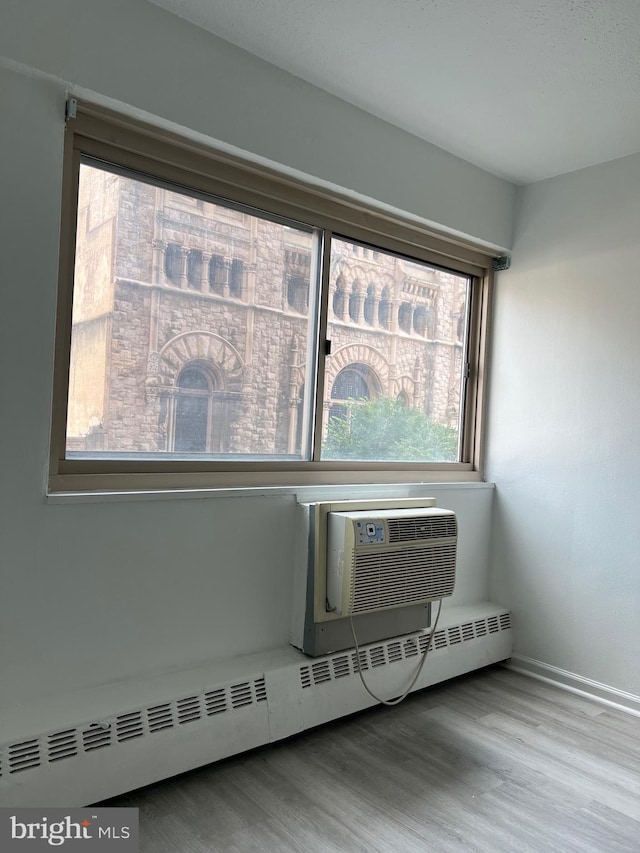 interior space featuring a baseboard heating unit, an AC wall unit, and hardwood / wood-style flooring