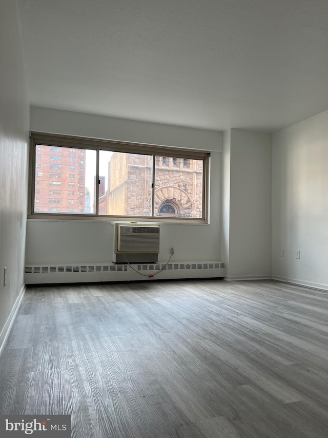 spare room featuring baseboard heating, wood-type flooring, and a wall mounted air conditioner