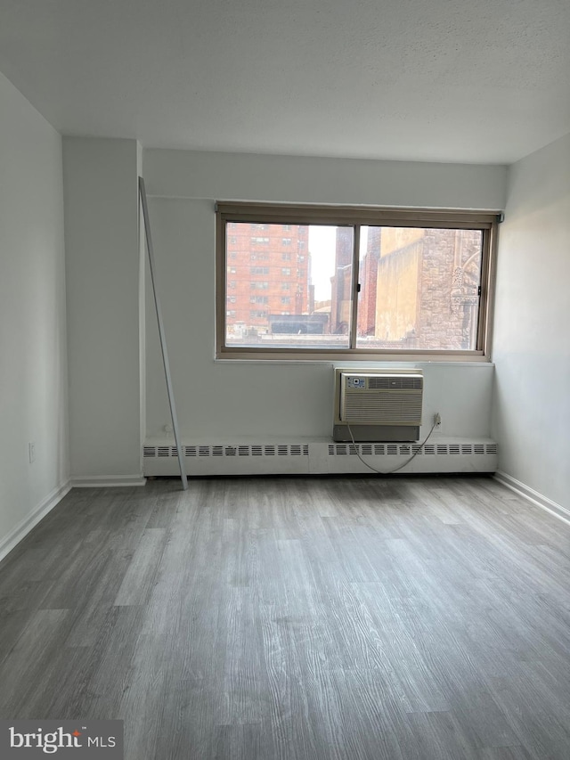 spare room with a baseboard heating unit, wood-type flooring, and a wall mounted AC