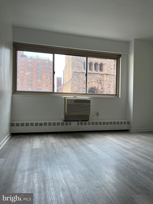 empty room featuring a baseboard heating unit, an AC wall unit, and hardwood / wood-style floors