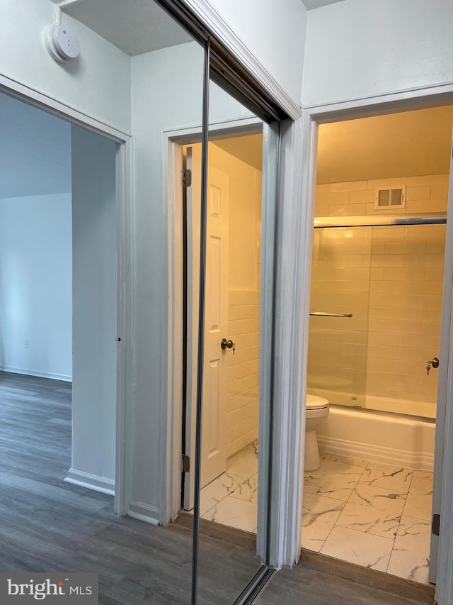 bathroom with wood-type flooring, toilet, and enclosed tub / shower combo