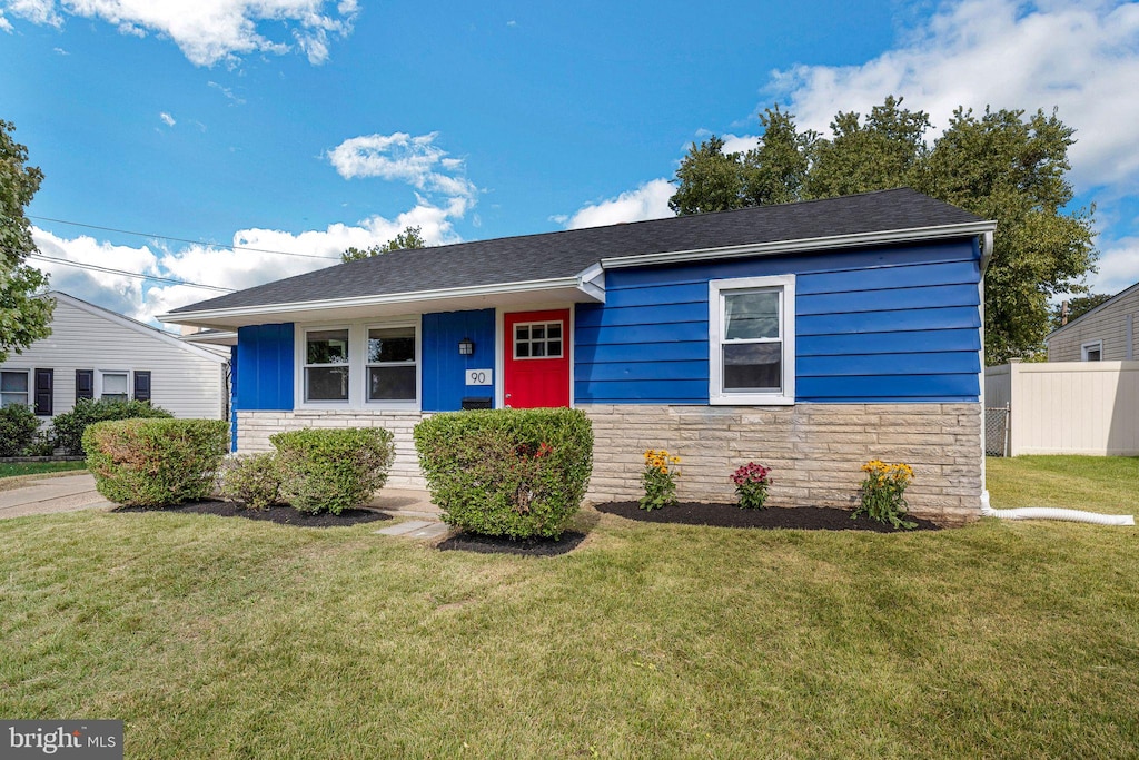 single story home with a front yard, stone siding, and fence