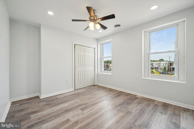 unfurnished bedroom with multiple windows, ceiling fan, a closet, and wood-type flooring