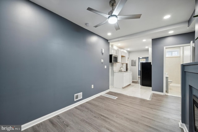 unfurnished living room with light wood-type flooring, sink, and ceiling fan