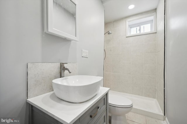 bathroom with tile patterned flooring, toilet, tiled shower, and vanity