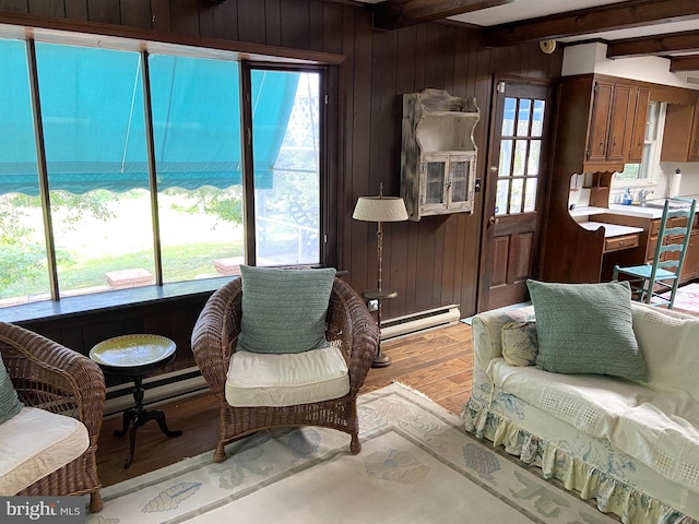 living room featuring wood walls, baseboard heating, beamed ceiling, and light hardwood / wood-style floors