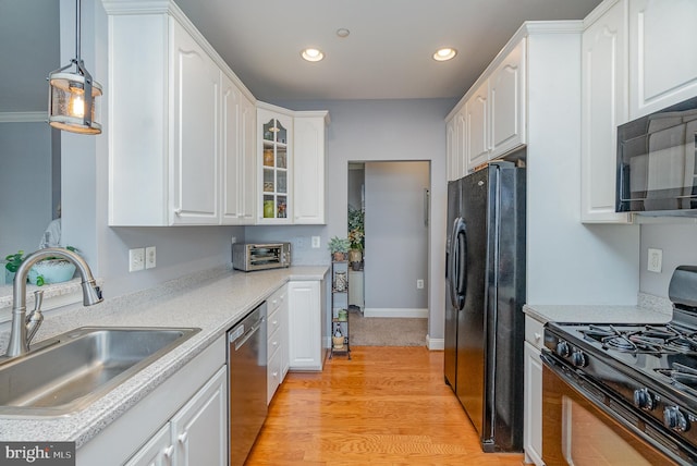 kitchen with hanging light fixtures, sink, black appliances, white cabinets, and light hardwood / wood-style floors