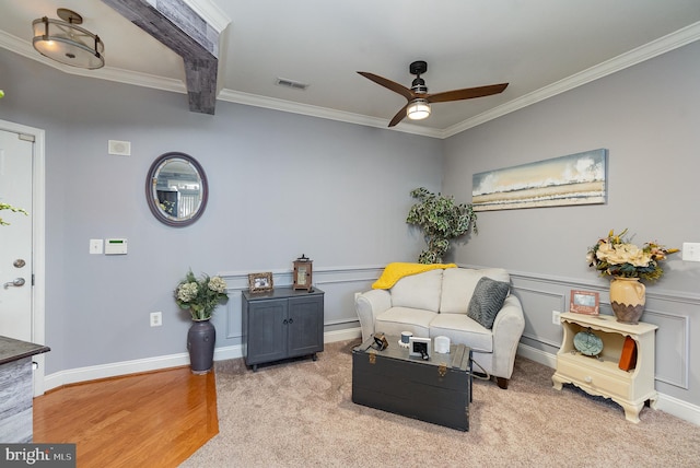 carpeted living room with crown molding, beamed ceiling, and ceiling fan