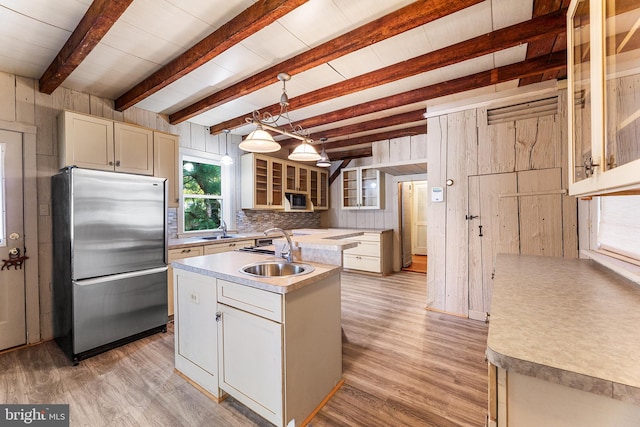 kitchen featuring sink, hanging light fixtures, light wood-type flooring, stainless steel fridge, and a kitchen island with sink