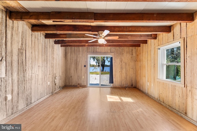 unfurnished room with beam ceiling, plenty of natural light, and light hardwood / wood-style floors