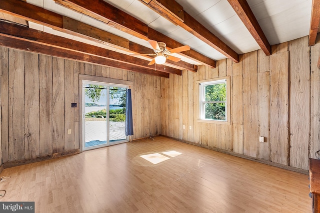 empty room featuring beamed ceiling, ceiling fan, wooden walls, and light hardwood / wood-style flooring