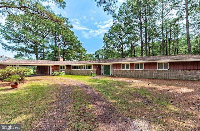 single story home featuring an attached carport, brick siding, board and batten siding, a front lawn, and a chimney