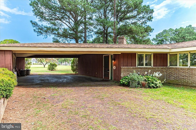 view of front of house with board and batten siding, brick siding, a chimney, and a carport