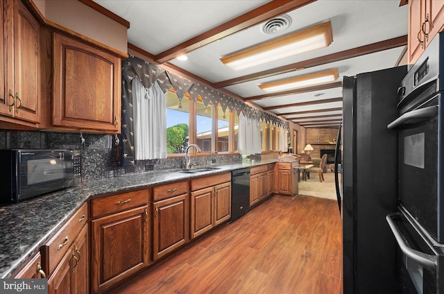 kitchen featuring visible vents, brown cabinets, wood finished floors, black appliances, and a sink