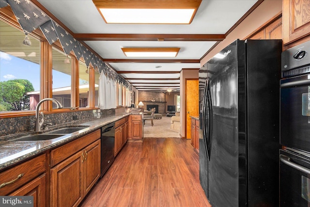 kitchen with a fireplace, a sink, dark wood-style floors, black appliances, and brown cabinetry