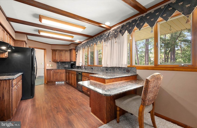 kitchen featuring brown cabinetry, a peninsula, a sink, under cabinet range hood, and beam ceiling