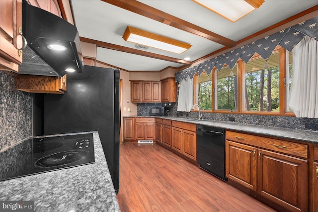 kitchen featuring brown cabinets, decorative backsplash, dark wood-type flooring, a sink, and black appliances