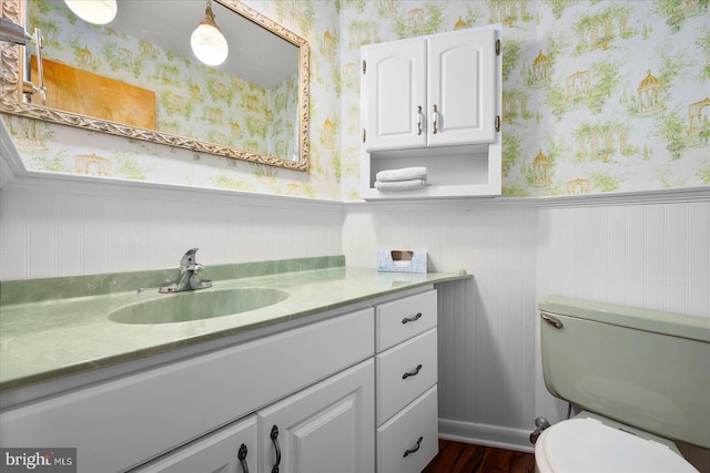 bathroom with wainscoting, vanity, toilet, and wallpapered walls