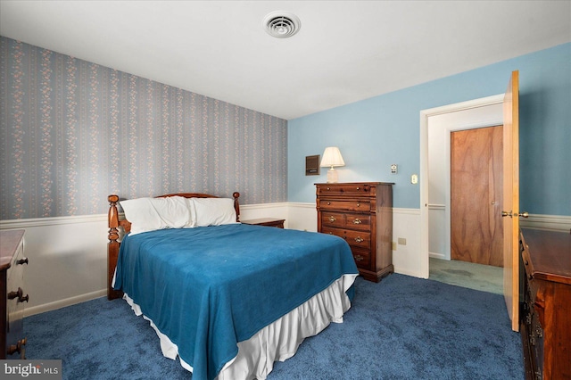 carpeted bedroom with a wainscoted wall, baseboards, visible vents, and wallpapered walls