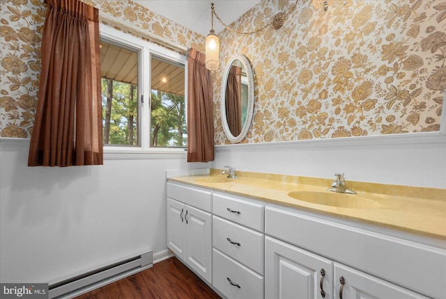 bathroom with a baseboard heating unit, double vanity, a sink, and wallpapered walls