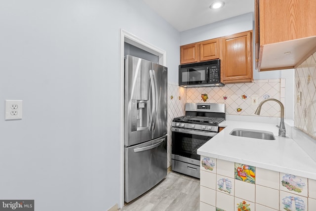 kitchen with appliances with stainless steel finishes, brown cabinets, a sink, light countertops, and backsplash