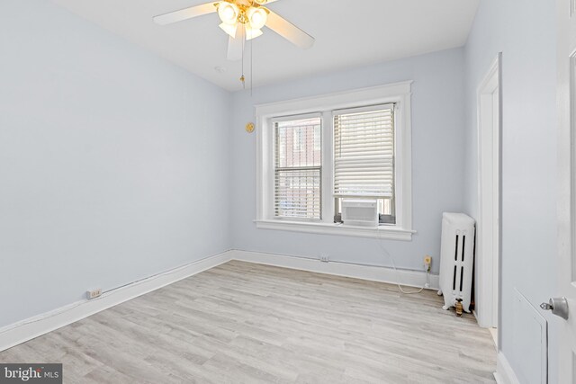 spare room featuring baseboards, ceiling fan, light wood finished floors, and radiator heating unit