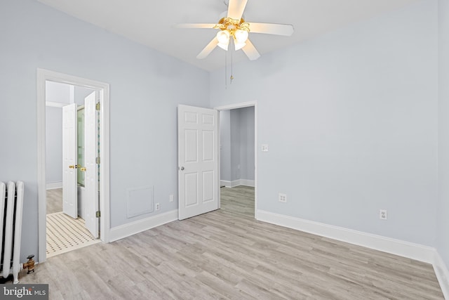 unfurnished bedroom with radiator, light wood-style flooring, ensuite bathroom, a ceiling fan, and baseboards