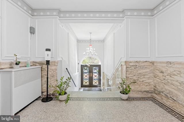 entryway with ornamental molding, a decorative wall, and an inviting chandelier