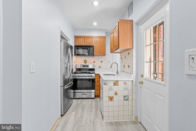 kitchen featuring a sink, light countertops, appliances with stainless steel finishes, decorative backsplash, and light wood finished floors