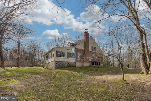 rear view of house with brick siding, a yard, a chimney, central AC unit, and a sunroom