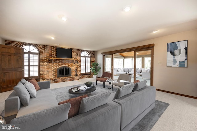 living area with a brick fireplace, brick wall, baseboards, and light colored carpet