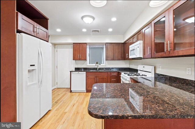 kitchen featuring dark stone countertops, white appliances, light wood-type flooring, sink, and kitchen peninsula