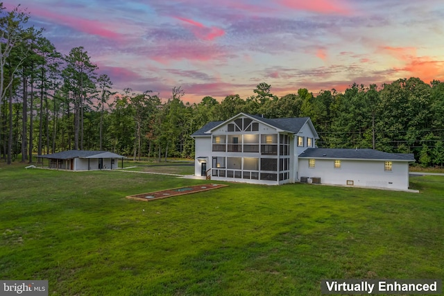 back house at dusk with a sunroom and a yard