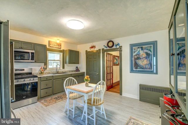 kitchen featuring radiator, green cabinets, appliances with stainless steel finishes, light hardwood / wood-style flooring, and sink