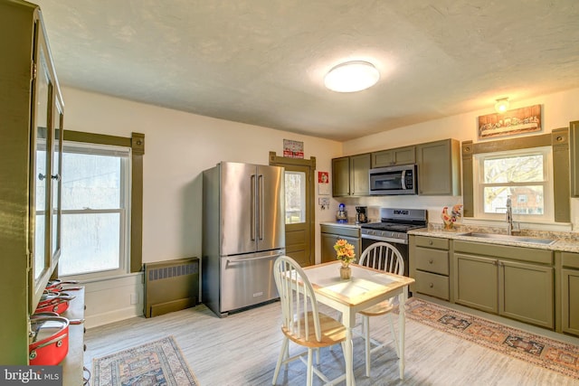 kitchen with radiator heating unit, light hardwood / wood-style flooring, appliances with stainless steel finishes, and sink