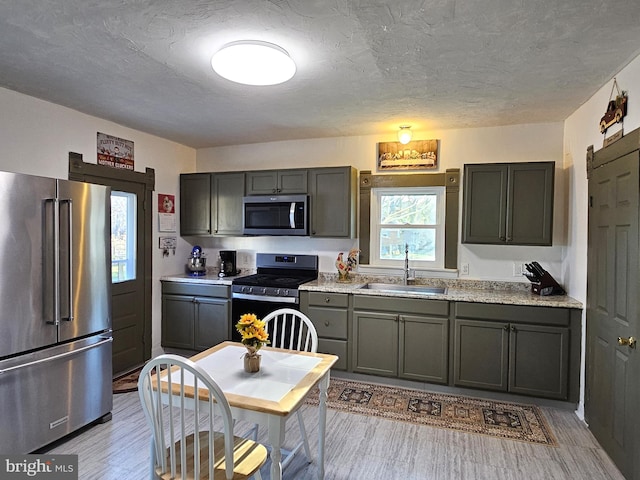 kitchen featuring light hardwood / wood-style flooring, light stone countertops, gray cabinets, stainless steel appliances, and sink