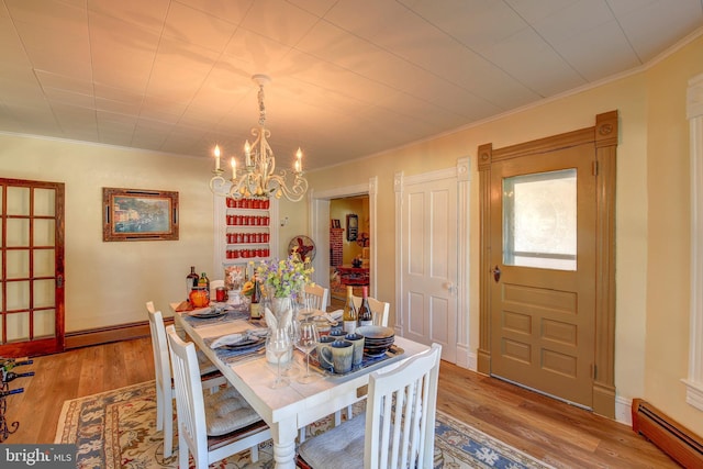 dining room with light wood-type flooring, ornamental molding, an inviting chandelier, and baseboard heating