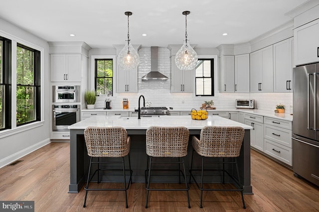 kitchen featuring a breakfast bar area, high end appliances, hanging light fixtures, a kitchen island with sink, and wall chimney range hood