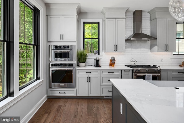 kitchen featuring wall chimney exhaust hood, light stone counters, appliances with stainless steel finishes, dark hardwood / wood-style flooring, and backsplash