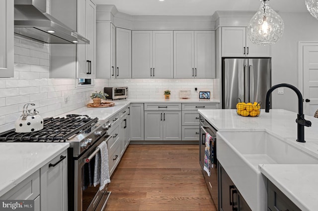 kitchen with light stone counters, wall chimney range hood, sink, and premium appliances