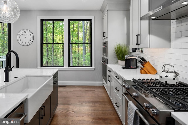 kitchen featuring white cabinetry, stainless steel appliances, light stone counters, and wall chimney range hood