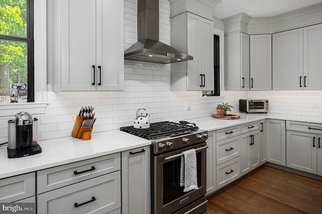 kitchen with stainless steel gas range, light stone counters, dark hardwood / wood-style floors, wall chimney range hood, and backsplash