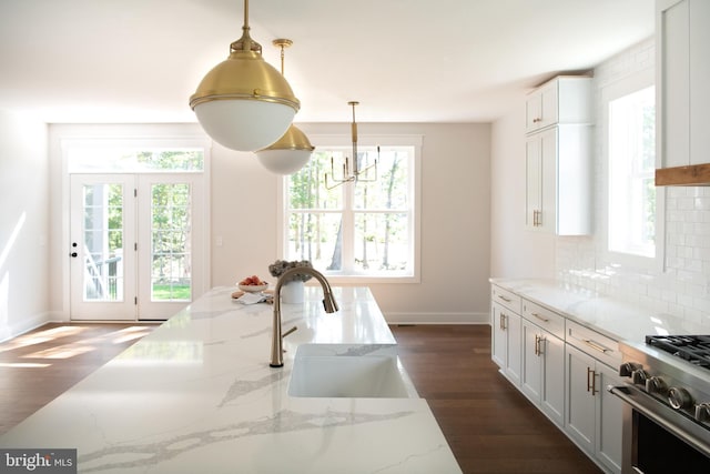 kitchen with sink, white cabinets, hanging light fixtures, light stone countertops, and dark wood-type flooring