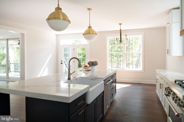 kitchen featuring sink, light stone countertops, an island with sink, white cabinets, and decorative light fixtures