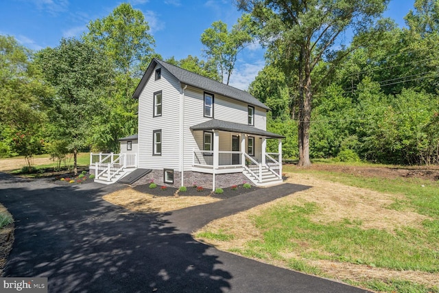 farmhouse inspired home with covered porch, aphalt driveway, and roof with shingles