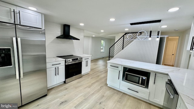 kitchen featuring wall chimney exhaust hood, white cabinetry, light hardwood / wood-style floors, light stone counters, and stainless steel appliances