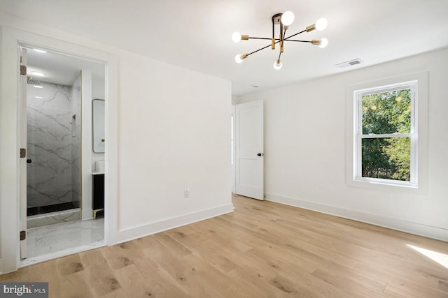 unfurnished bedroom featuring light wood-type flooring, ensuite bathroom, and a chandelier