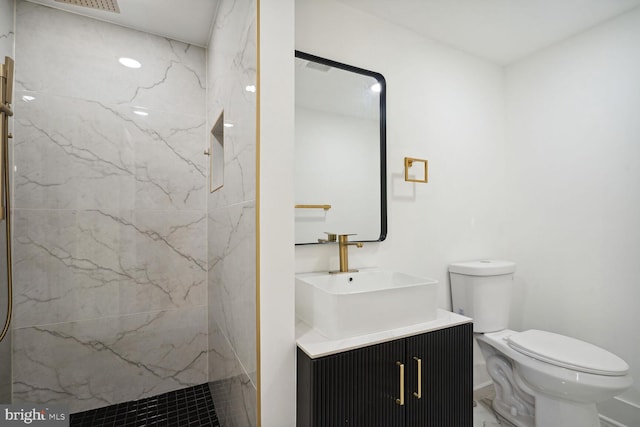 bathroom with toilet, tiled shower, and vanity