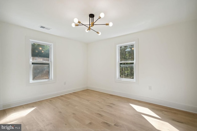 empty room featuring light wood-type flooring and a notable chandelier