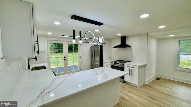 kitchen with appliances with stainless steel finishes, sink, light stone countertops, wall chimney range hood, and hanging light fixtures